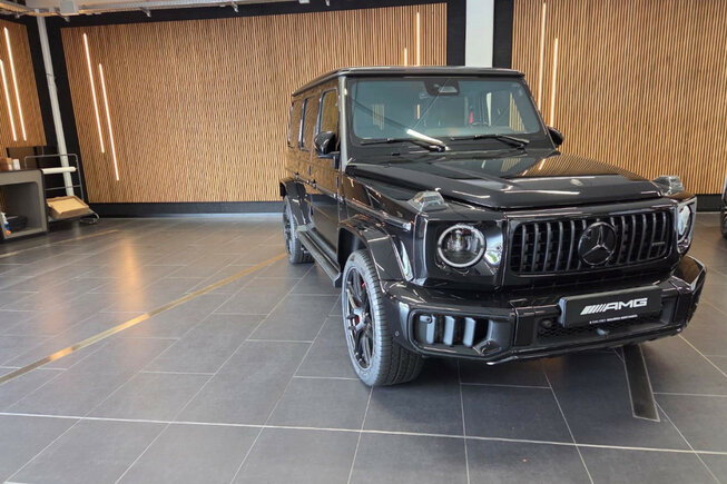 Schwarzer Mercedes-AMG in einem Ausstellungsraum mit stilvoller Wandgestaltung aus JOKA Paro Akustikpaneelen in Eiche und vertikal eingelassenen LED-Leuchten.