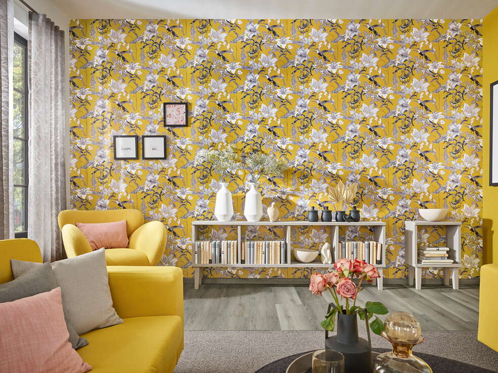 Detailaufnahme einer Akzentwand im Wohnzimmer, die mit der gelben JOKA Tapete mit Blumenmuster verziert ist.