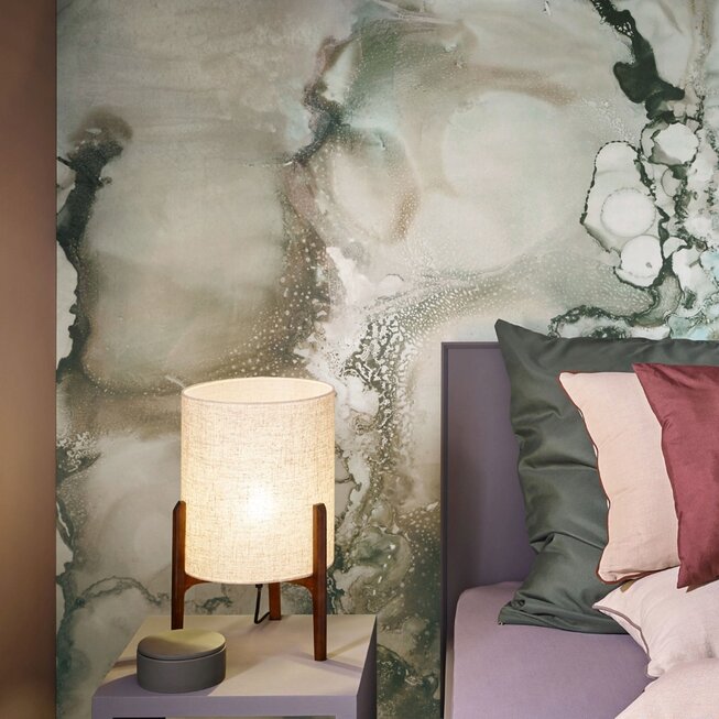 Schlafzimmer mit floraler JOKA Wandtapete in Naturtönen, grünem Teppichboden und farblich abgestimmten Kissen.