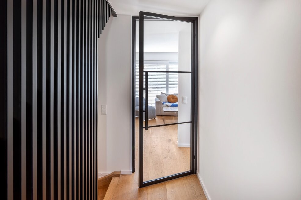 Schwarze JOKA Lofttür mit Glasfüllung in einem modernen Flur neben einer dunklen Wandverkleidung.