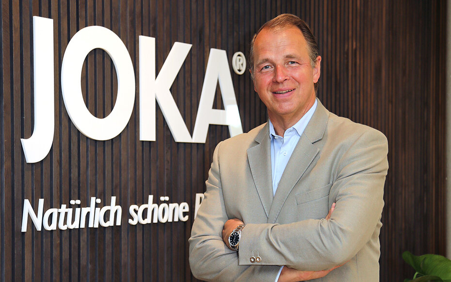 Bild von Geschäftsführer Jörg Jordan, der vor einer Wand mit JOKA Akustikpaneele und dem Logo steht.
