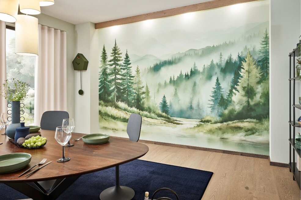 Essbereich mit großflächiger JOKA Wandtapete mit Waldmotiv, rundem Esstisch und blauem Teppich auf hellem Parkettboden.