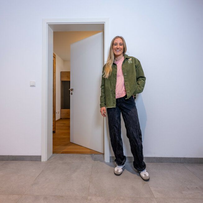 Bewohnerin steht im Wohnbereich mit JOKA Holzboden und Holztüren, hell und modern eingerichtet.