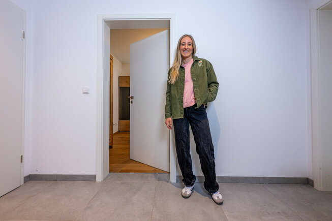 Bewohnerin steht im Wohnbereich mit JOKA Holzboden und Holztüren, hell und modern eingerichtet.