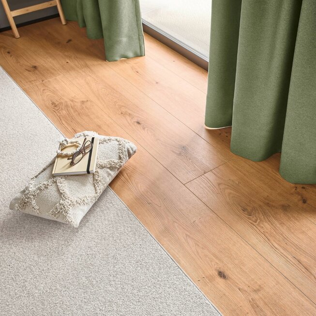 Detailbild von JOKA Lamitboden und abgepasstem Teppich. Am Rand sind noch Gardinen zu erkennen in frischen grünlichen Farben.