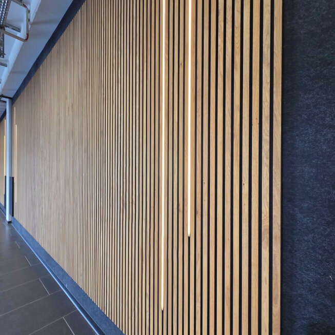 Detailansicht einer Wandverkleidung mit JOKA Paro Akustikpaneelen in Eiche, kombiniert mit vertikal integrierter LED-Beleuchtung in einem modernen Autohaus.