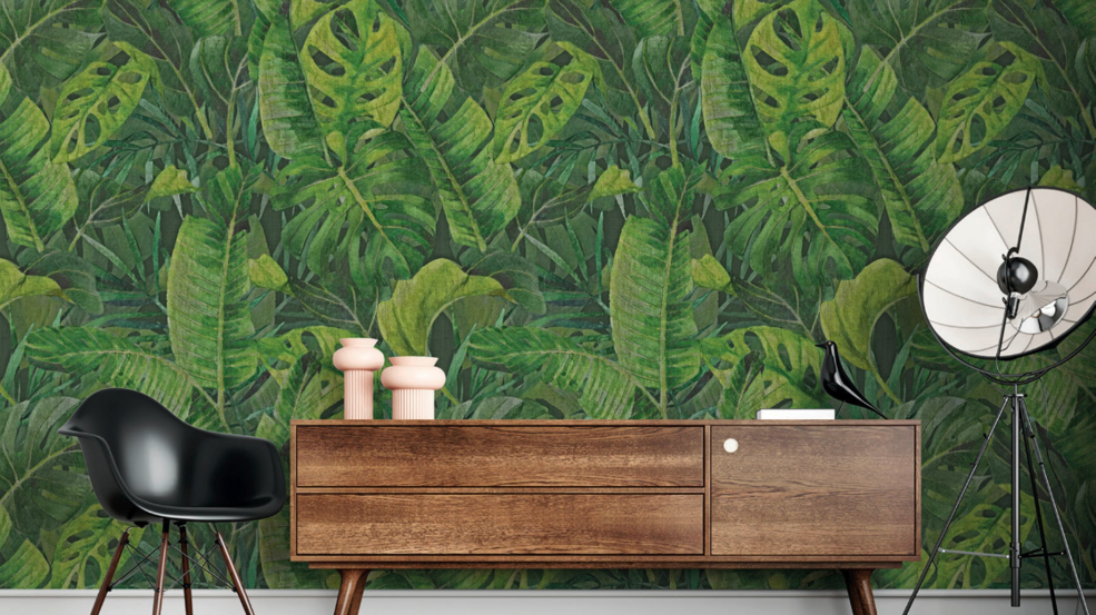 Nahaufnahme einer grünen JOKA Tapete mit Blattmotiv und einem Sideboard davor.