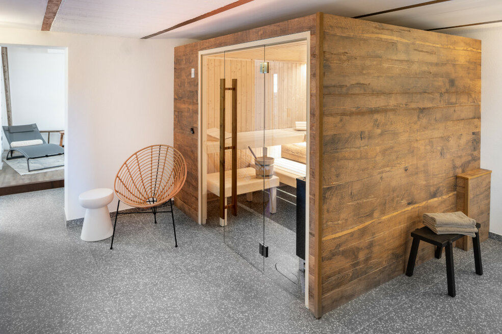 Gemütlicher Ruhebereich mit Blick in eine integrierte Sauna, kombiniert mit Designboden in Grau und dekorativer Holzverkleidung.