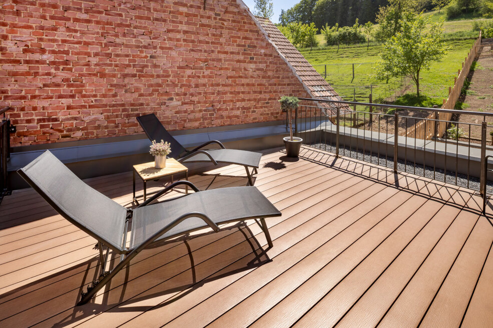 Sonnige Dachterrasse mit Blick ins Grüne, ausgestattet mit zwei modernen Liegen auf einem gepflegten Terrassendielenboden.