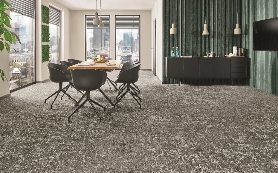 Raumbild eines Meeting-Raums in dem ein großer Tisch mit Stühlen steht. Die eine Hälfte der Wände ist mit grünen Wandpaneelen behängt und der ganze Raum hat grauen Teppichboden.