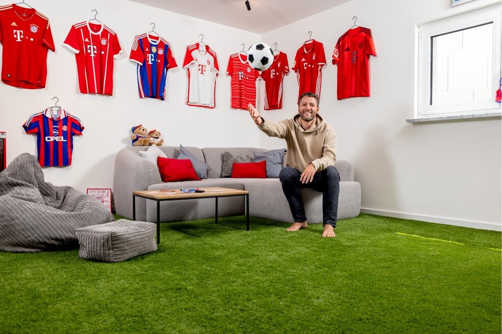 Wohnbereich mit grünem JOKA Kunstrasen, Sitzsäcken und Sporttrikots an der Wand.
