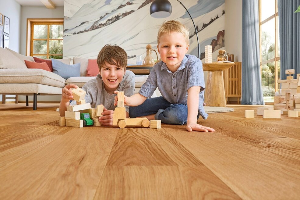 Kinder liegen auf dem JOKA Naturholzbodens Kjare in einem Wohnzimmer.