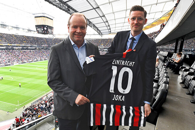 Zwei Personen im Stadion präsentieren ein Trikot mit der Nummer 10, JOKA-Partnerschaft.