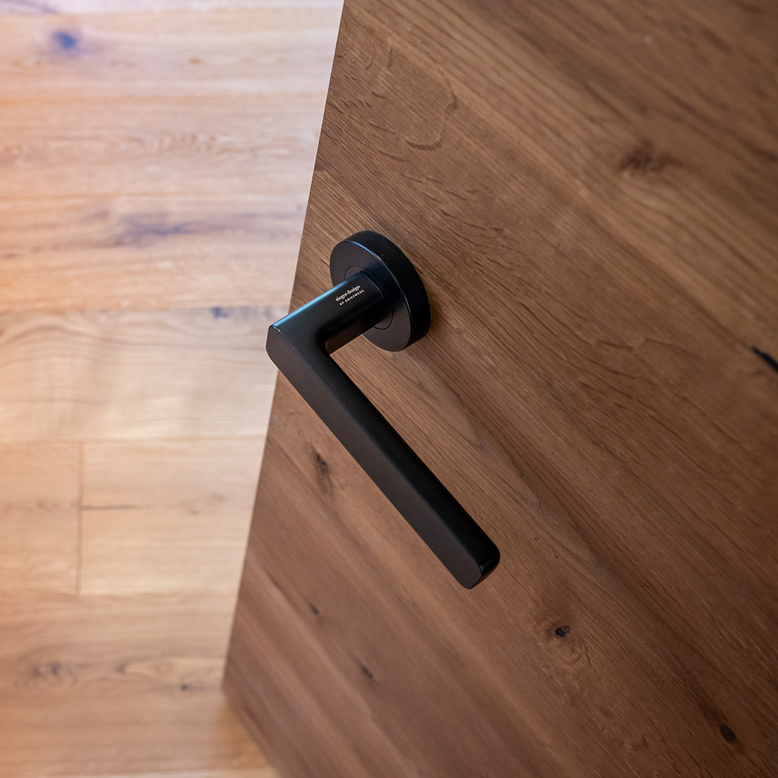 Detailbild eine schwarzen Türklinke und Tür in Holzoptik.