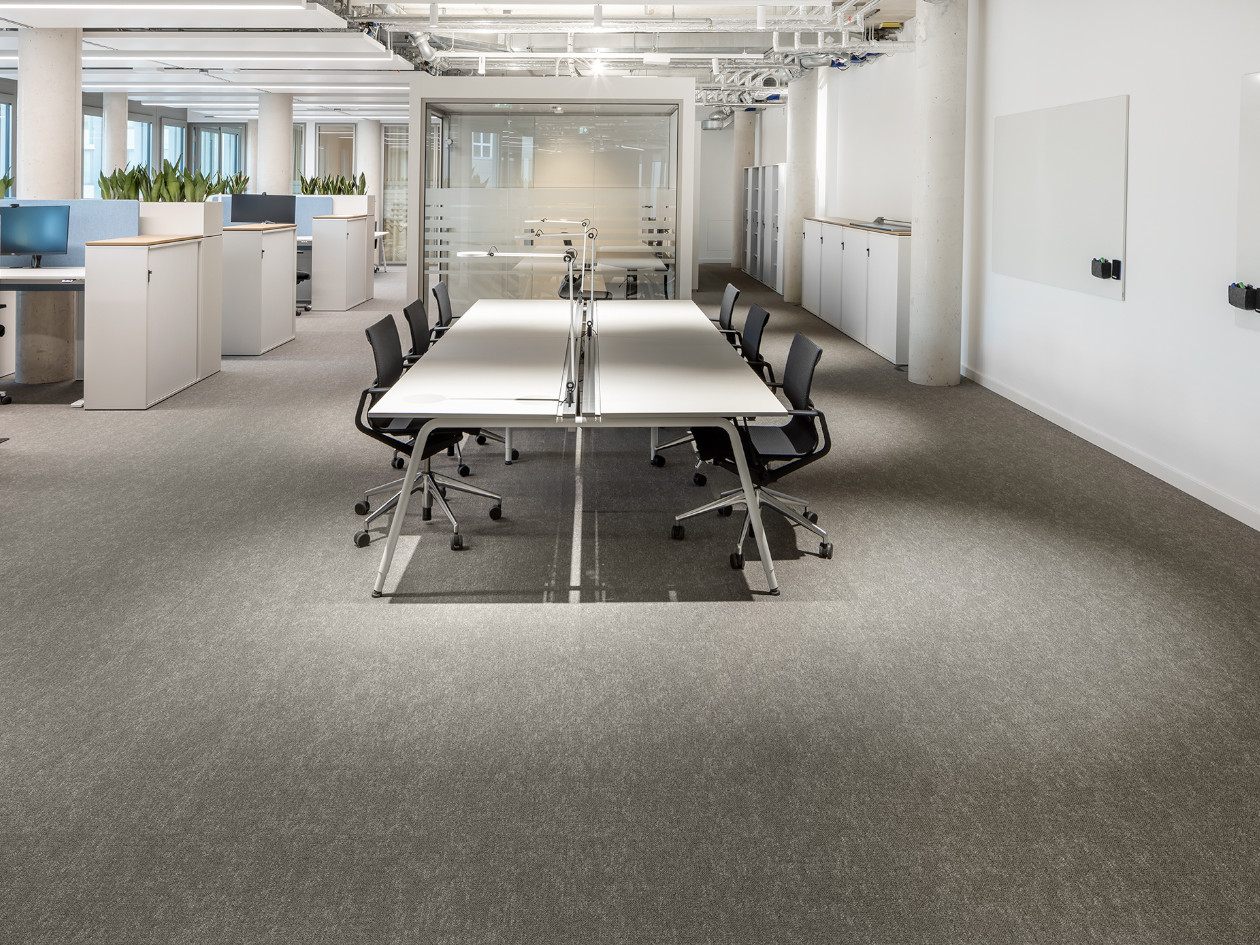 Moderner Konferenzraum mit grauen Stühlen, Glastrennwänden und einem langen Konferenztisch.