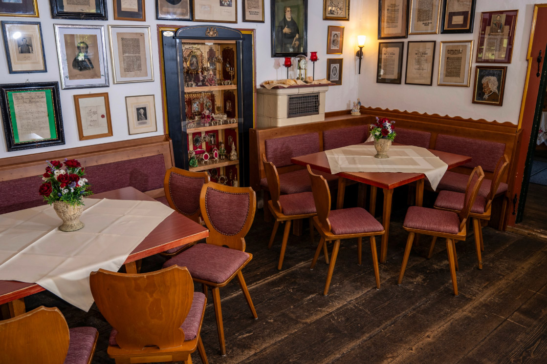 Ein gemütlich eingerichteter Essbereich in einem Restaurant mit Holzmöbeln und Wänden, die mit Bildern dekoriert sind. Dunkler Holzboden und rot gepolsterte Stühle verleihen dem Raum eine warme Atmosphäre.