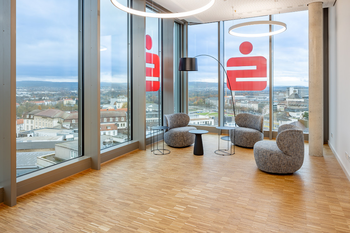 Panorama-Lounge-Bereich mit Parkettboden, großen Fenstern und Blick auf das Sparkassen-Logo.