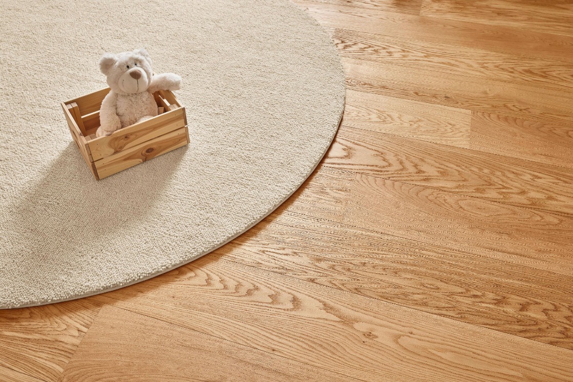 Detailbild eines Fußbodens, auf dem ein runder, abgepasster beige-farbener Teppich von JOKA liegt.