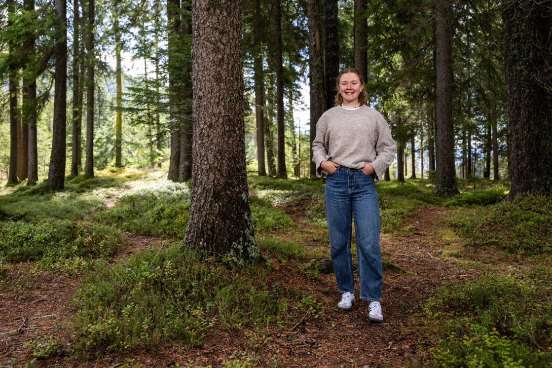 JOKA Athletin Selina Grotian steht in einem Waldgebiet, umgeben von hohen Bäumen. Sie trägt ein Lächeln auf den Lippen, während sie in die Kamera schaut.