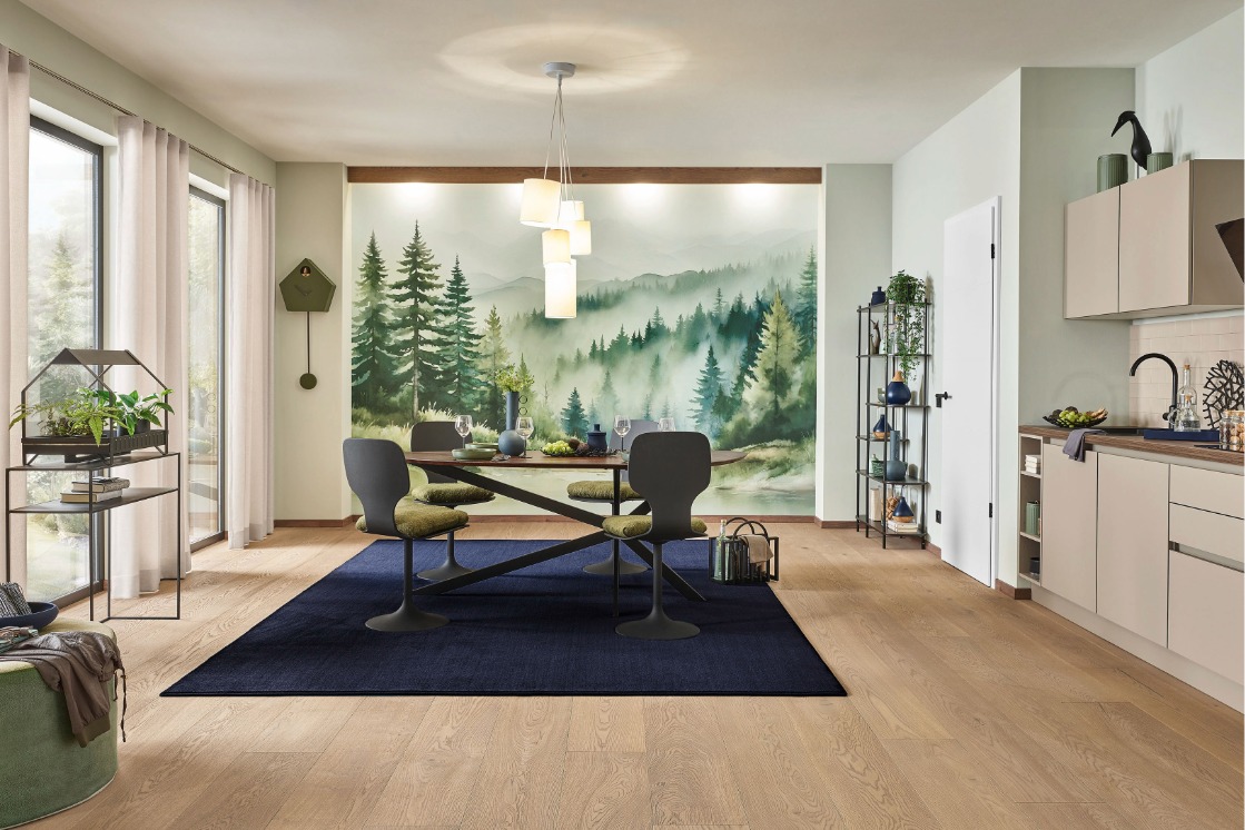 Offener Wohn- und Essbereich mit JOKA Parkett Calgary Eiche Barrique, blauem Teppich und großflächiger Wandtapete mit Waldmotiv.