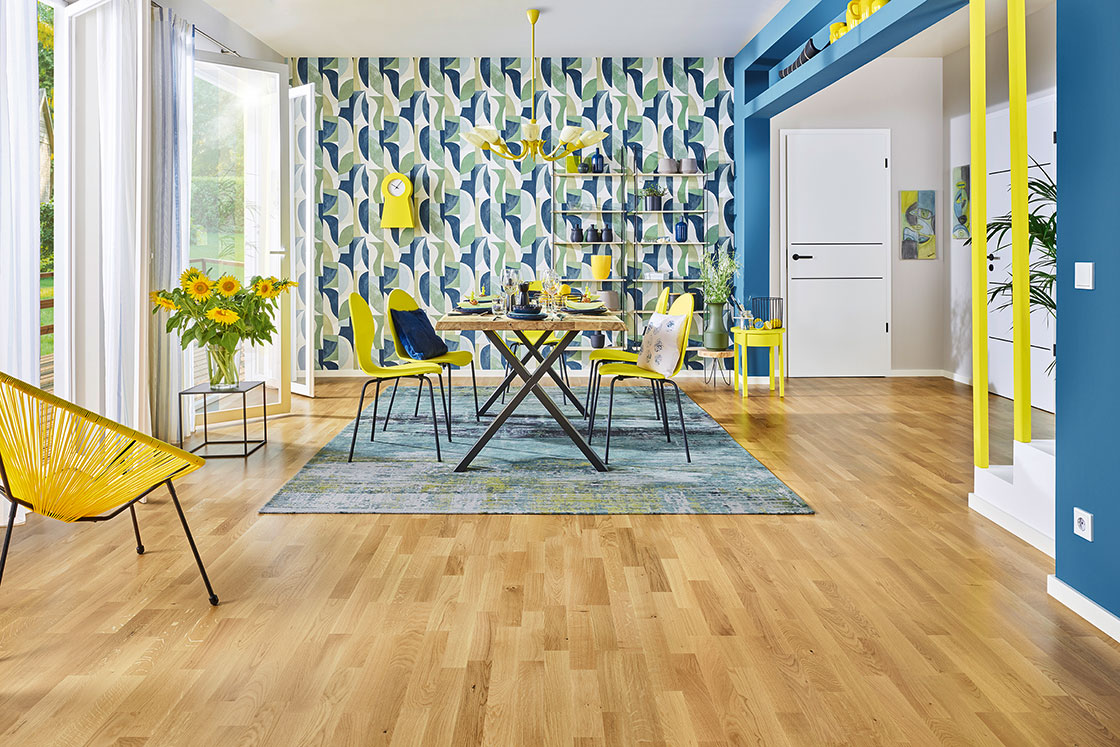 Raumbild eines Esszimmers, was durch blaue und gelbe JOKA Gardinen, Tapete und Teppich nach der Lebensfreude Wohnidee eingerichtet ist.