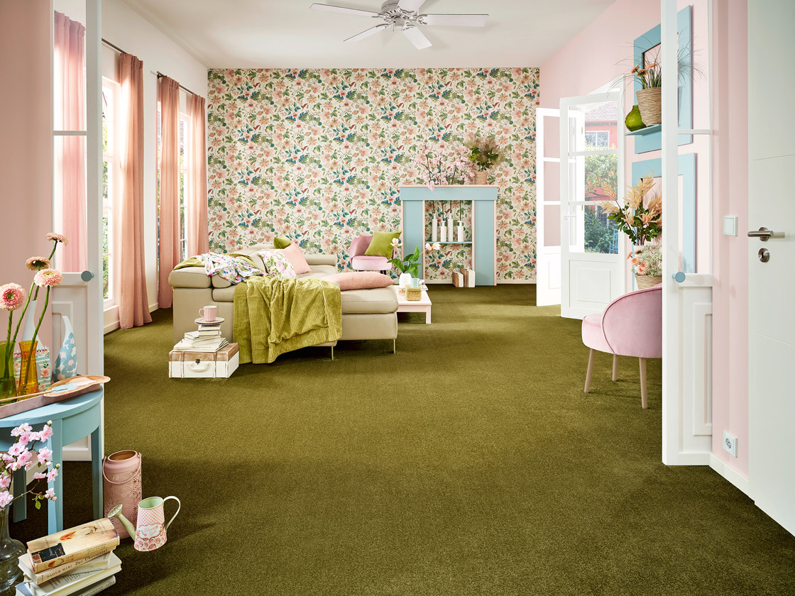 Raumbild eines bunten Wohnzimmers - Pink gemusterte JOKA Tapeten zieren die Wände, der grüne JOKA Teppich den Boden.