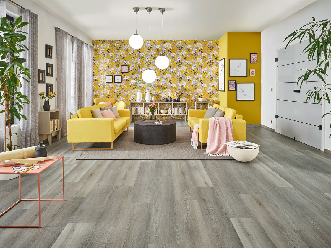 Raumbild eines grau gelb eingerichteten Wohnzimmers – graues JOKA Laminat und gelbe Wohnstoffe verleihen dem Raum seinen Charme.
